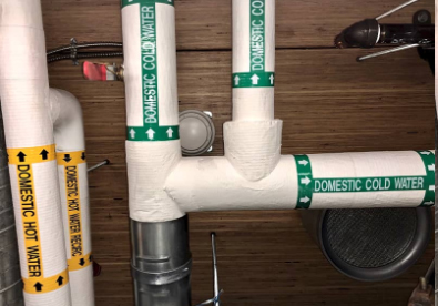Insulated piping system labeled with Domestic Cold Water and Domestic Hot Water pipe markers in a mechanical room