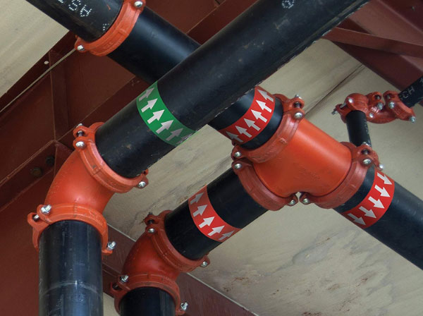 Industrial black piping system with red grooved couplings and directional flow markers indicating pipe flow direction